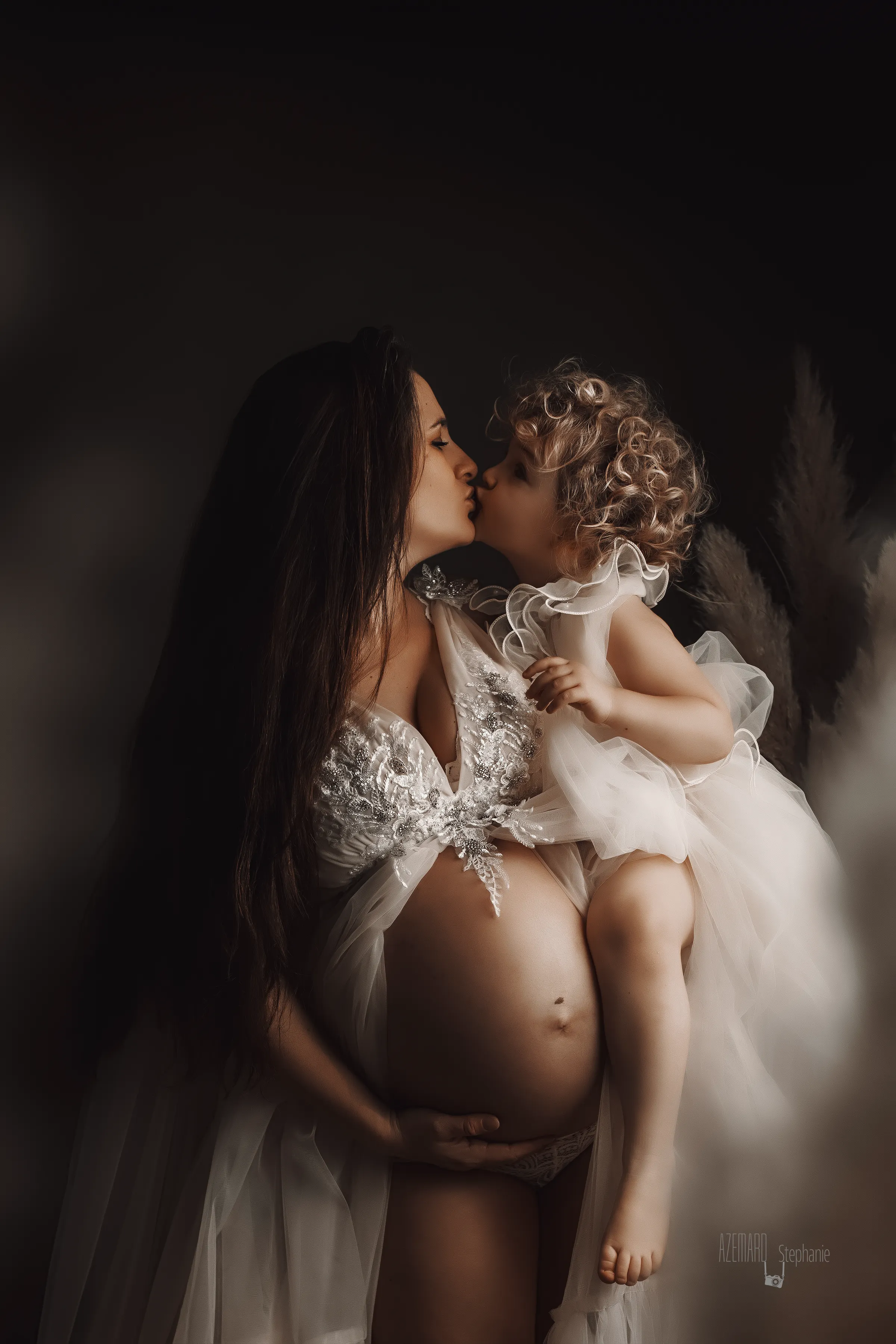 - Stéphanie Azémard Photographe Montpellier Photo grossesse maman enceinte embrassant sa fille habillée en ange en studio fond sombre, photographe maternité Montpellier Stéphanie Azémard