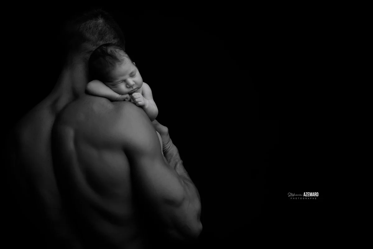 Photo nouveau-né endormi sur l'épaule de son papa en noir et blanc studio fond noir, photographe maternité Montpellier Stéphanie Azémard
