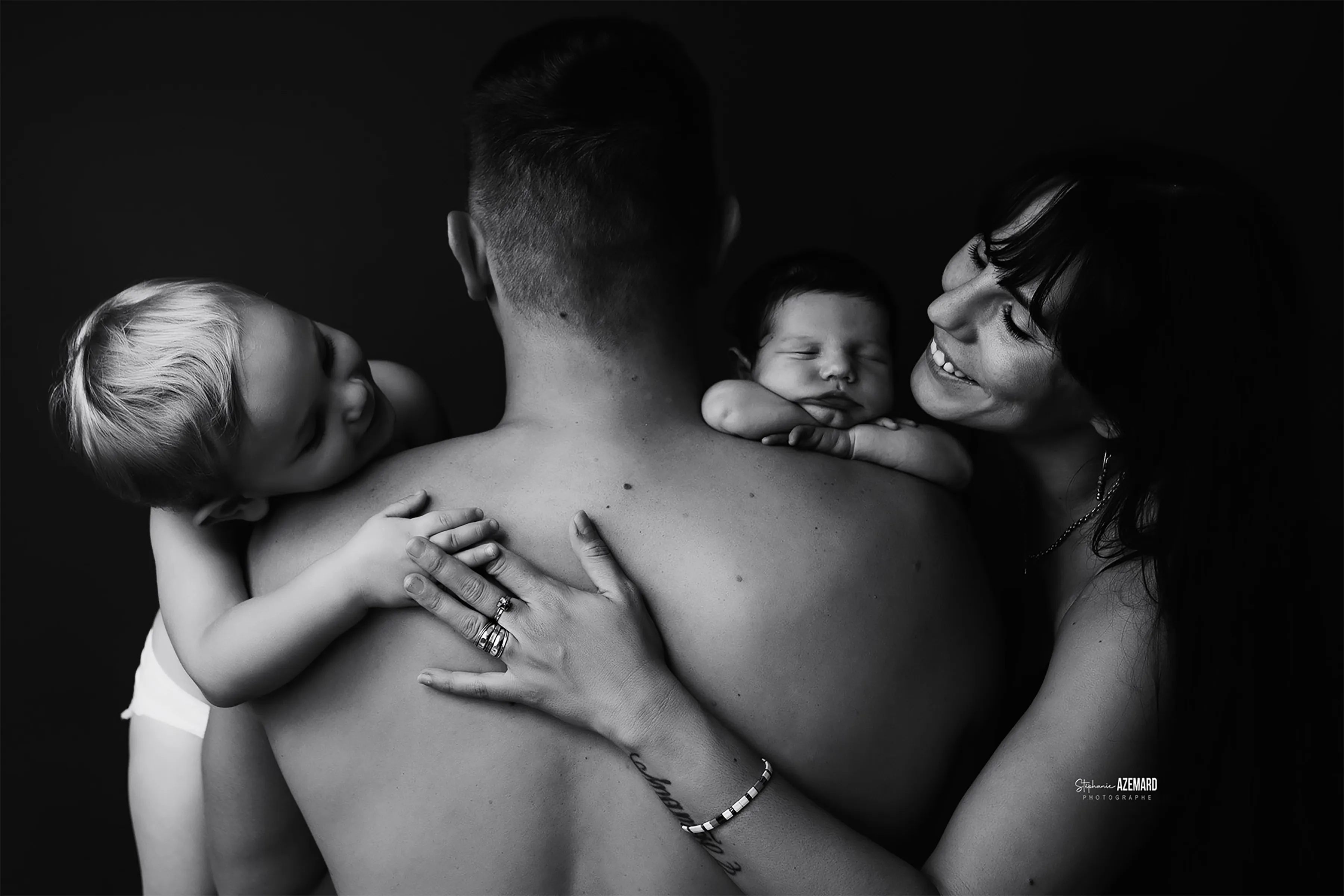 - Stéphanie Azémard Photographe Montpellier Photo famille parents avec nouveau-né endormi et grand enfant blond en noir et blanc studio, photographe maternité Montpellier Stéphanie Azémard