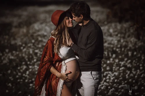 © Stéphanie Azémard — Photographe maternité Montpellier Photo grossesse couple enlacé en extérieur champ bohème, future maman ventre arrondi chapeau rouge, photographe maternité Montpellier Stéphanie Azémard