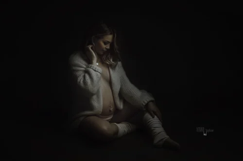 © Stéphanie Azémard — Photographe maternité Montpellier Photo grossesse future maman assise en gilet laine blanc lumière sombre studio fond noir, photographe maternité Montpellier Stéphanie Azémard