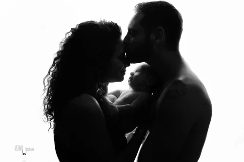 © Stéphanie Azémard — Photographe maternité Montpellier Photo famille parents s'embrassant avec nouveau-né éveillé en silhouette contre-jour noir et blanc fond blanc, photographe maternité Montpellier Stéphanie Azémard