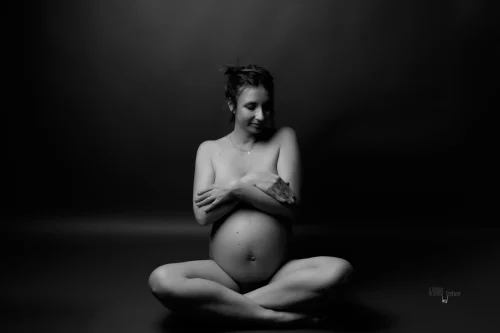 © Stéphanie Azémard — Photographe maternité Montpellier Photo grossesse future maman assise en tailleur au sol en noir et blanc studio fond sombre, photographe maternité Montpellier Stéphanie Azémard