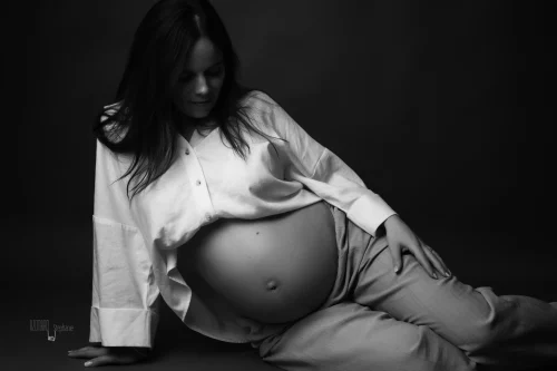 © Stéphanie Azémard — Photographe maternité Montpellier Photo grossesse future maman chemise blanche ouverte assise au sol en noir et blanc studio fond sombre, photographe maternité Montpellier Stéphanie Azémard