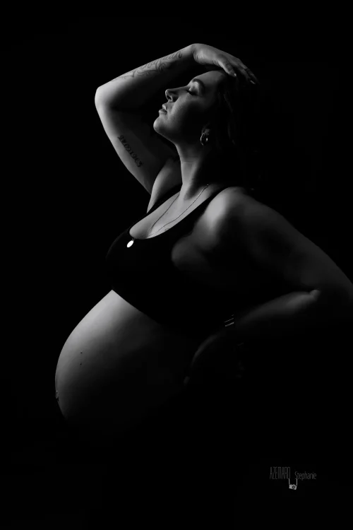 © Stéphanie Azémard — Photographe maternité Montpellier Photo grossesse future maman de profil tatouages tête levée ventre arrondi en noir et blanc studio fond noir, photographe maternité Montpellier Stéphanie Azémard