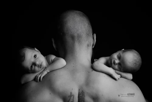 © Stéphanie Azémard — Photographe maternité Montpellier Photo jumeaux nouveau-nés posés sur les épaules de leur papa de dos en noir et blanc studio fond noir, photographe maternité Montpellier Stéphanie Azémard