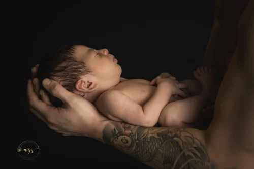 © Stéphanie Azémard — Photographe maternité Montpellier Photo nouveau-né endormi dans les mains tatouées de son père en studio fond noir, photographe maternité Montpellier Stéphanie Azémard