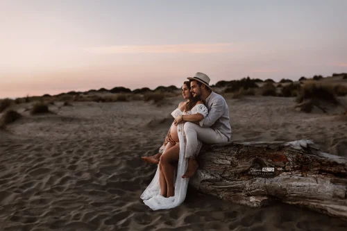 © Stéphanie Azémard — Photographe maternité Montpellier Photo grossesse couple assis sur tronc bois dans les dunes au coucher de soleil, photographe maternité Montpellier Stéphanie Azémard