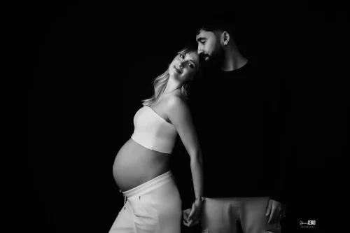 © Stéphanie Azémard — Photographe maternité Montpellier Photo grossesse couple élégant noir et blanc studio fond noir, future maman ventre arrondi appuyée contre son partenaire, photographe maternité Montpellier Stéphanie Azémard