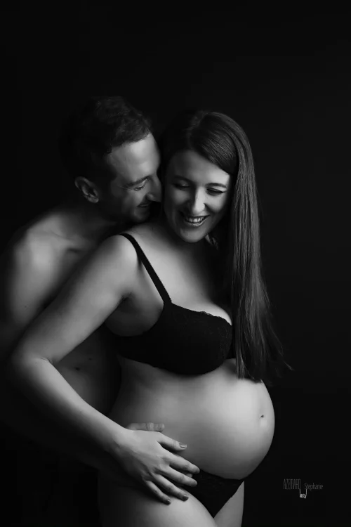 © Stéphanie Azémard — Photographe maternité Montpellier Photo grossesse couple souriant et complice en noir et blanc studio fond noir, future maman ventre arrondi, photographe maternité Montpellier Stéphanie Azémard