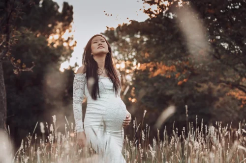 Séance photo de grossesse en extérieur réalisée par Stéphanie Azémard, photographe maternité à Montpellier : femme enceinte en robe blanche dentelle dans les herbes folles au coucher du soleil. Séance photo grossesse en pleine nature au coucher du soleil, femme enceinte en robe blanche dentelle, photographe maternité Montpellier