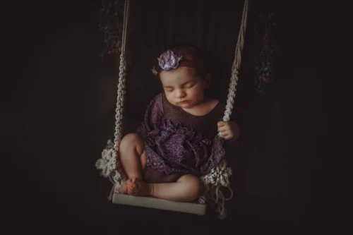 Séance naissance en studio — Stéphanie Azémard photographe naissance Montpellier Séance photo naissance bébé endormi sur une balançoire en studio, robe violette et bandeau fleuri, photographe naissance Montpellier