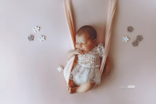Séance newborn poétique en studio — Stéphanie Azémard photographe naissance Montpellier Séance photo newborn bébé endormi dans un hamac rose avec fleurs décoratives, robe dentelle blanche, photographe naissance Montpellier