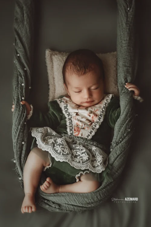 Séance photo naissance newborn réalisée par Stéphanie Azémard, photographe naissance à Montpellier : bébé endormi dans un hamac vert avec robe dentelle fleurie vintage. Séance photo newborn bébé endormi dans un hamac vert en studio, robe dentelle fleurie, photographe naissance Montpellier