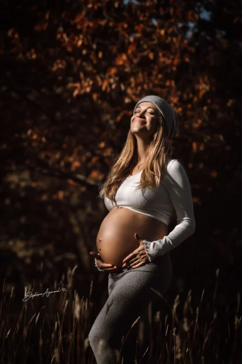 Femme enceinte au soleil d'automne, yeux fermés, mains sur le ventre