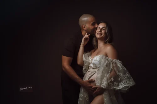 Future maman en robe de dentelle embrassée par son compagnon en studio