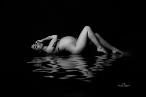 © Stéphanie Azémard — Photographe maternité Montpellier Photo grossesse artistique future maman allongée en noir et blanc avec reflet eau studio fond noir, photographe maternité Montpellier Stéphanie Azémard
